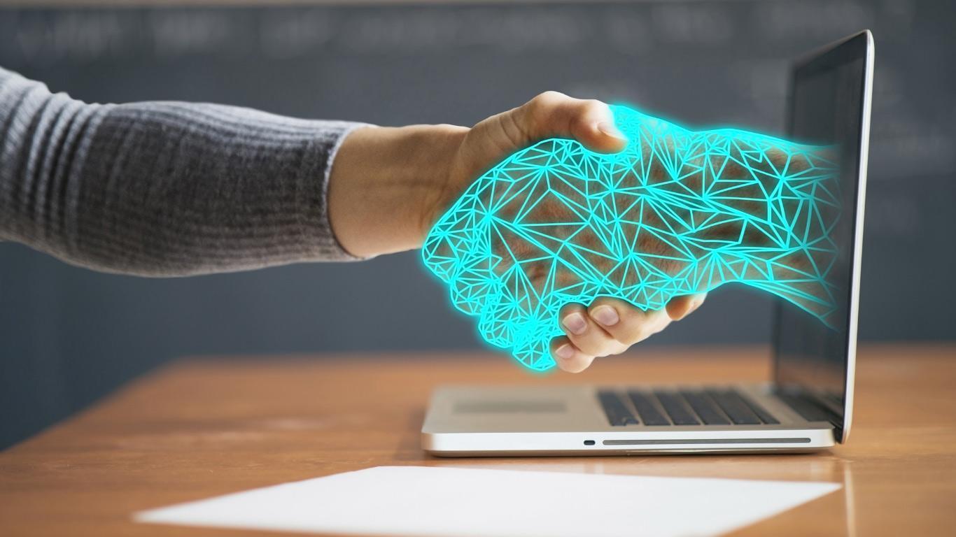 Zusammenarbeit mit Oracle Partner | Innconcepts IT GmbH Ein Händedruck zwischen einer realen Hand und einer digitalen, geometrischen Hand, die aus einem Laptop-Bildschirm kommt.